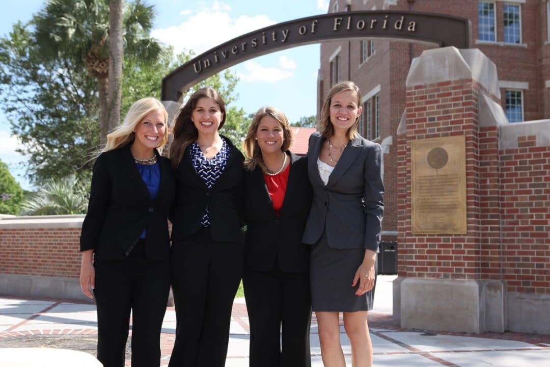 Four students pose in front of UF Warrington campus gateway