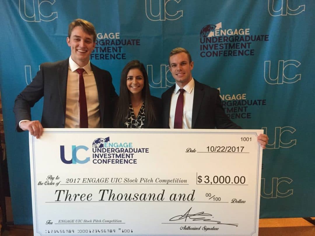 Three finance students hold a large check for $3,000 from a stock pitch competition