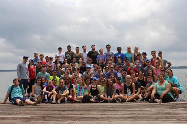Large group of student members of the Heavener Leadership Challenge pose for a photo on a dock by a lake