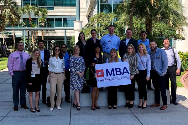Students and staff from the UF MBA program pose for a photo outside of the Raymond James offices while holding a UF MBA banner
