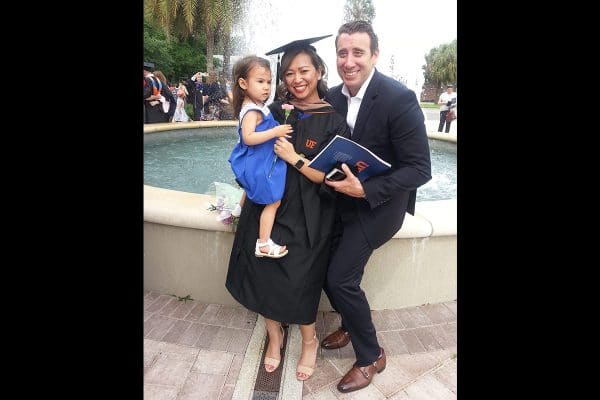 London Tawfik in a grad cap and gown pose with her daughter and husband