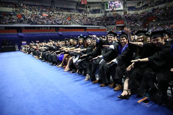 Students in graduation regalia doing the Gator chomp in the O'Connell Center at the UF Commencement ceremony