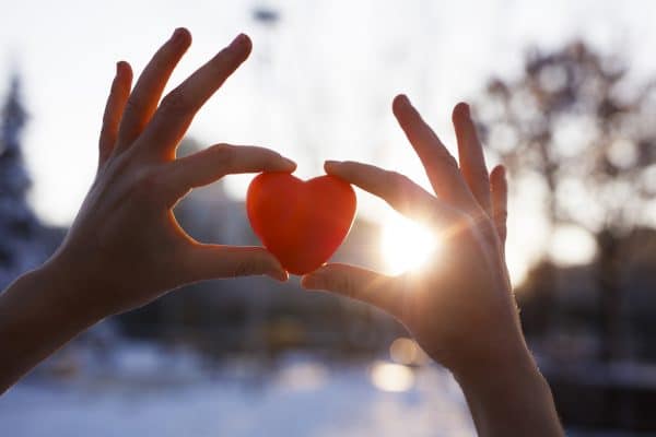 Woman holding heart-shaped red snowball, close-up of hands