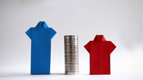Blue and red shirts made of paper with piles of coins in between. The concept of gender employment and wage gap in the enterprise.