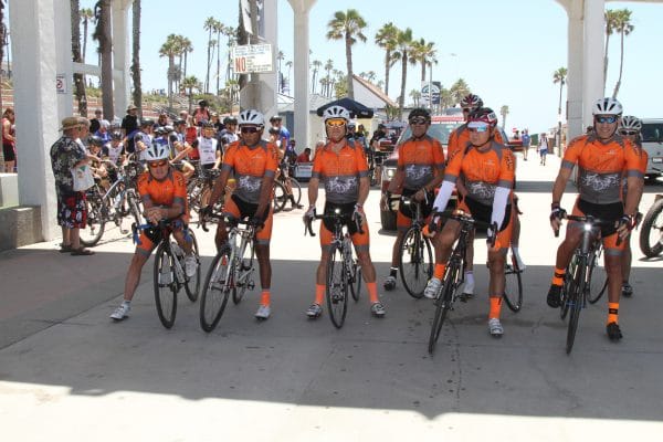 A line of men in orange bike gear on road bikes.