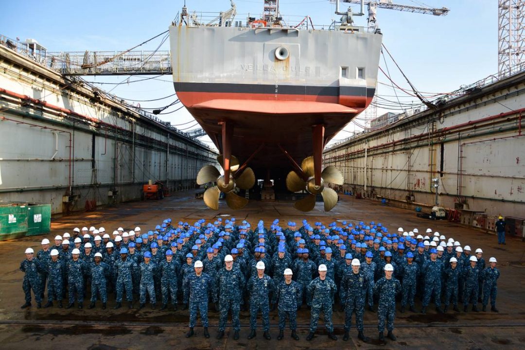 Large group of uniformed soldiers stand in formation in front of a large ship