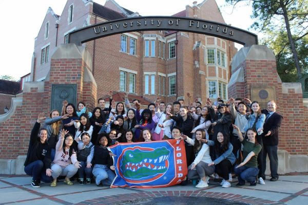 Group of students doing the Gator Chomp while holding a UF flag in front of Heavener Hall