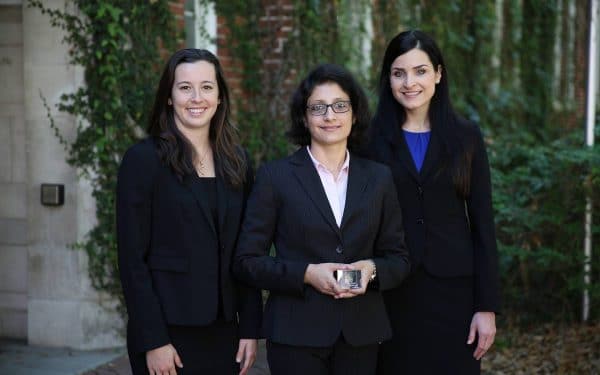 Three female students in suits pose for a photo with their trophy
