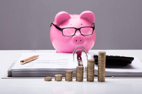 Piggy bank wearing glasses looking at paper and a calculator with stacks of coins in front