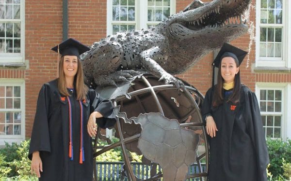 Angel and Morgan Pinkerton stand next to the Gator Ubiquity Statue in their graduation caps and gowns.