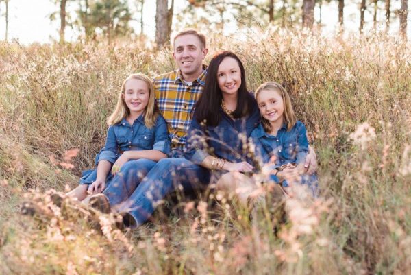 Daniel Hunt and his wife and two daughter sit in a field for a family photo.