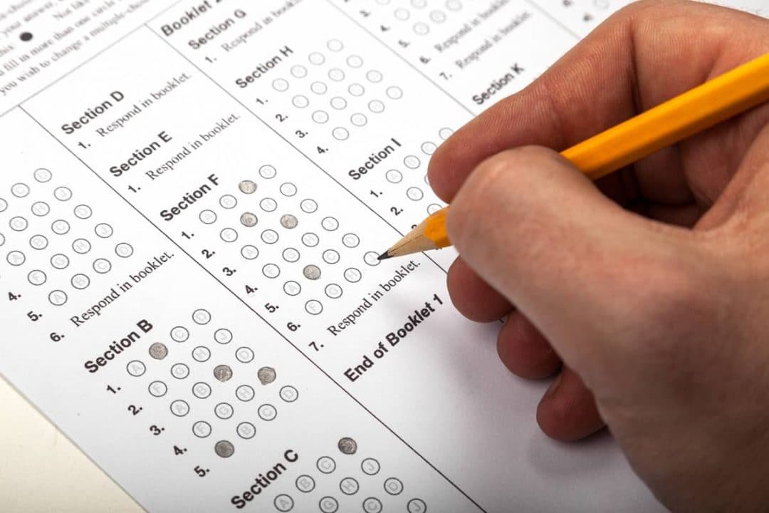 Close up of a hand holding a pencil while filling in bubbles on a standardized test answer sheet