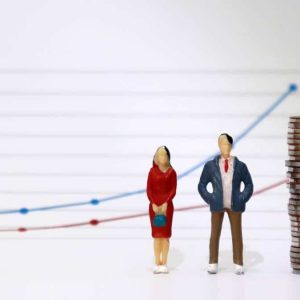 A miniature couple standing next to a pile of coins with a linear graph. The concept of the wage gap between men and women, which grows larger over time.