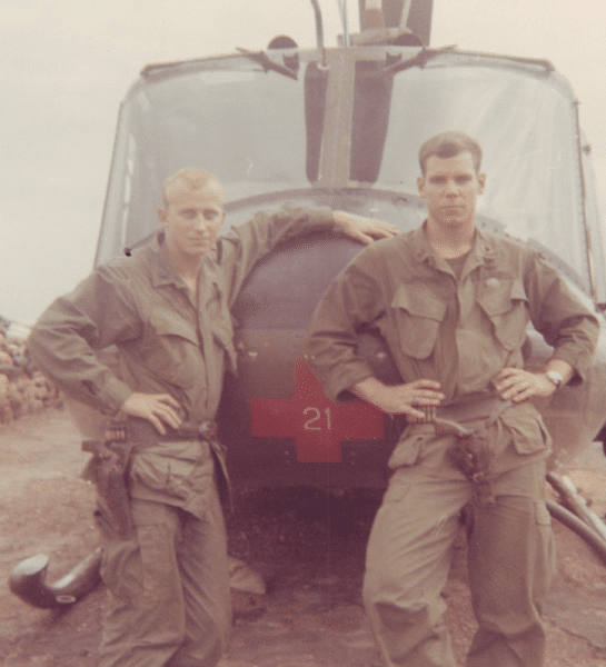 Art Jacobs, an Air Rescue Pilot, stands in front of a helicopter with another serviceman in Vietnam