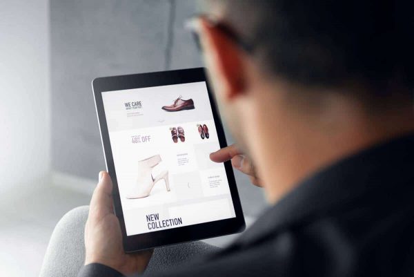 Male hand is browsing an online shop on digital tablet which is selling shoes.