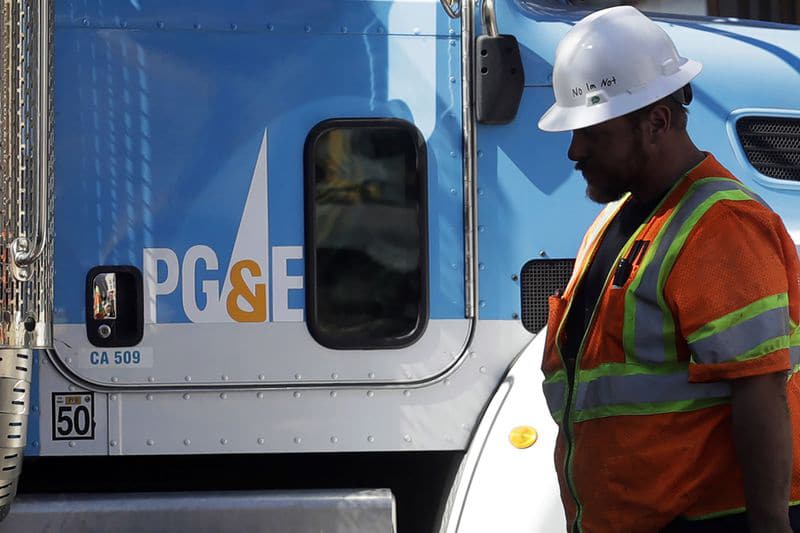 A worker with PG&E stands next to a PG&E utility truck