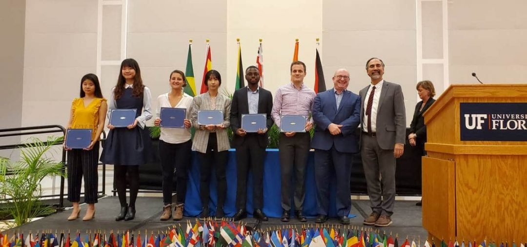 Six students stand with awards alongside two international programs directors