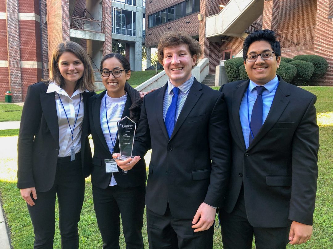Four students in business suits pose with their glass trophy from an ethics case competition