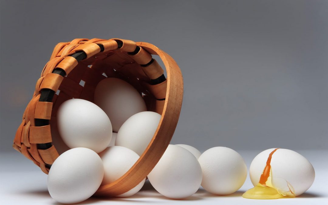 A small brown basket turned on its side with white eggs falling out. One of the eggs is broken.