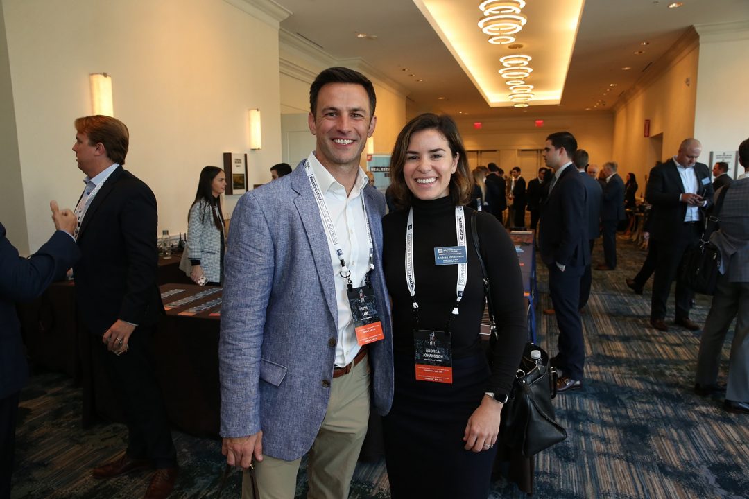 Man in suit poses with woman in suit at a conference