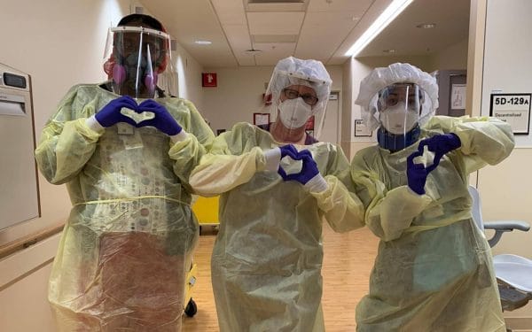 Three medical workers in protective equipment making hearts with their hands.