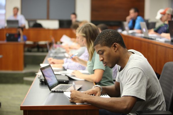 Side view of a row of students looking down while taking notes in class