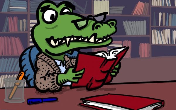 Cartoon alligator sitting at a desk reading a book. A large bookshelf filled with books sits behind him. There are two pens and another book on his desk.