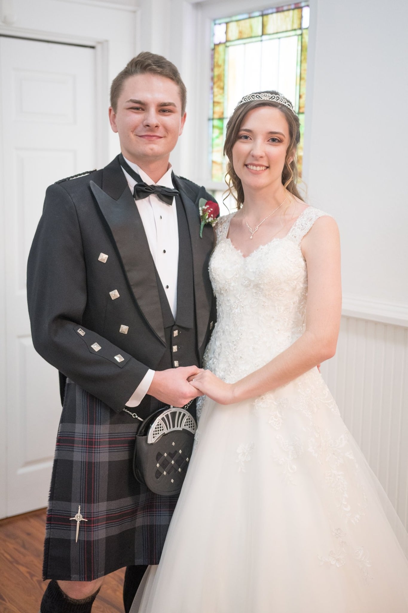 Leia Wojciechowski and her husband pose for a wedding portrait. He wears a Scottish kilt and she wears a white wedding dress.