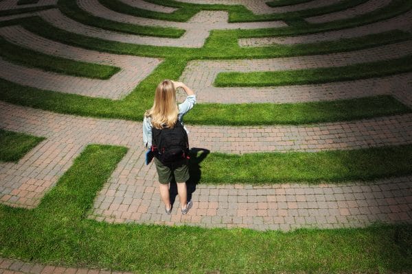 A woman student stands looking through the puzzling maze of schooling and the education system, forecasting the way forward and searching for the path to her goal. Concept of student facing uncertainty to their education, life and future career.