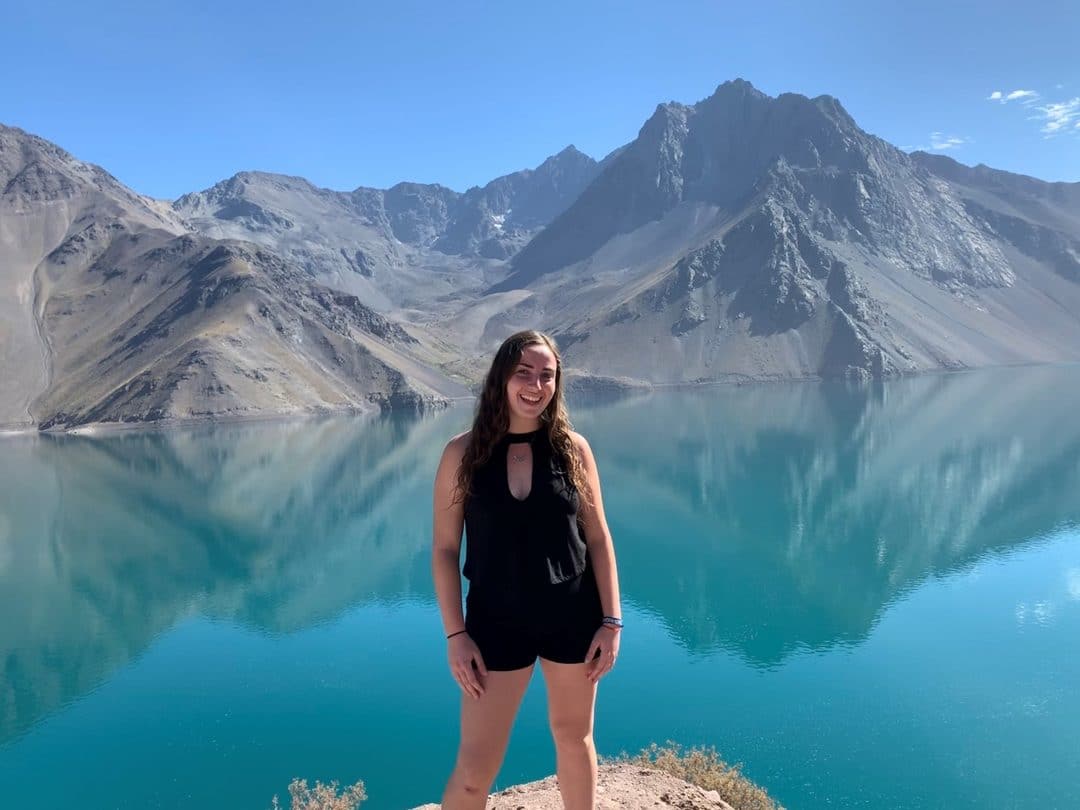 Iara Dircie stands in front of a large blue lake and mountains in Chile
