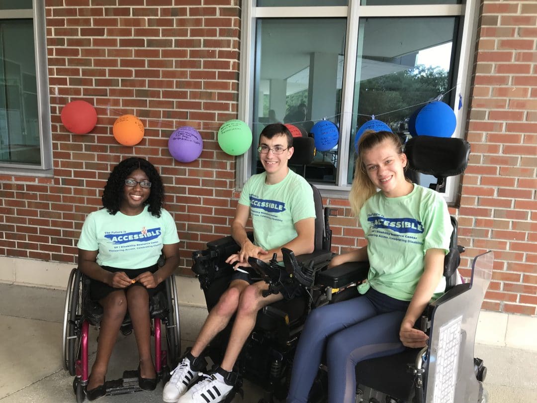 Three wheelchair-using UF students pose for a photo wearing shirts that say "The future is accessible"
