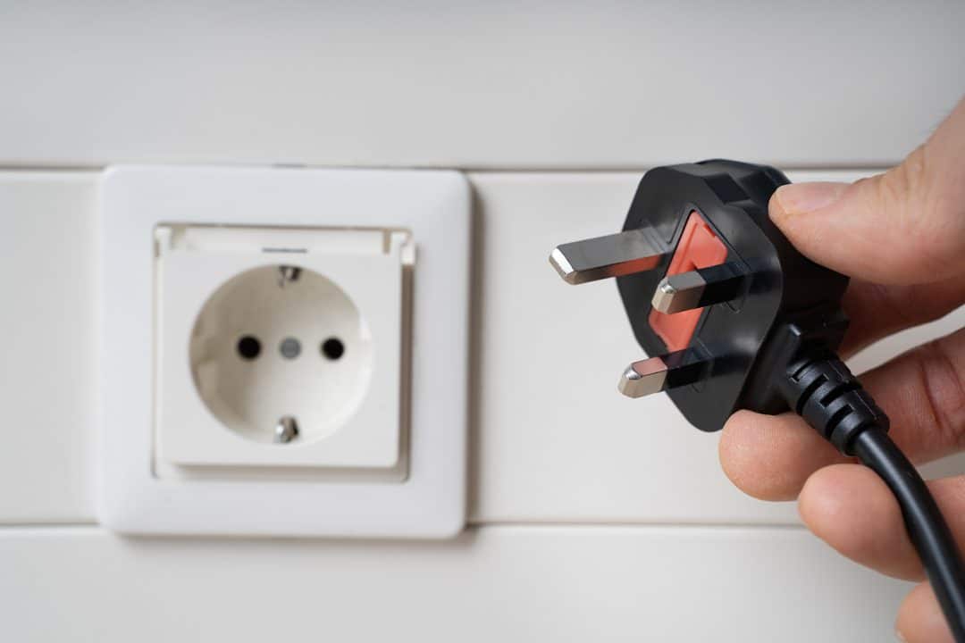 Hand Holding Incompatible AC Plug Near Wall Socket