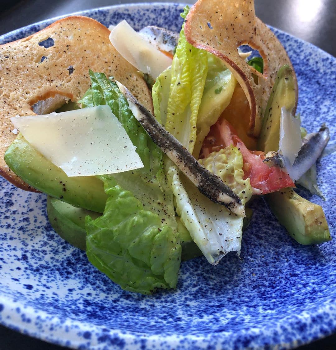 Close up of a Caesar salad with a bagel chip, tomatoes, anchovies and lettuce.
