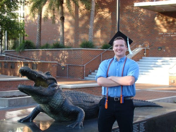 Jacob Schuster poses with his graduation cap next to an alligator statue.