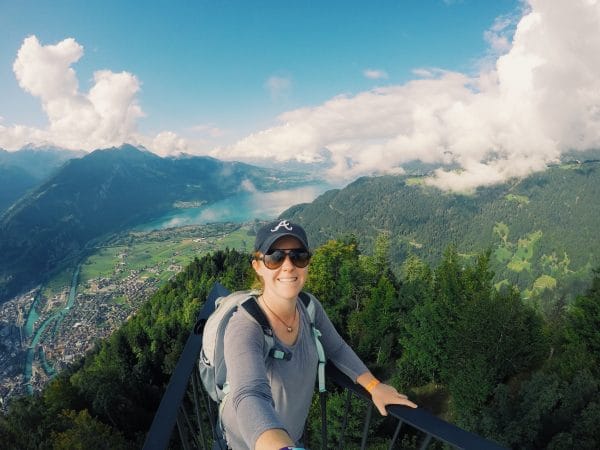 Stevie Faulk takes a photo with a selfie stick with the mountains of Switzerland in the background.