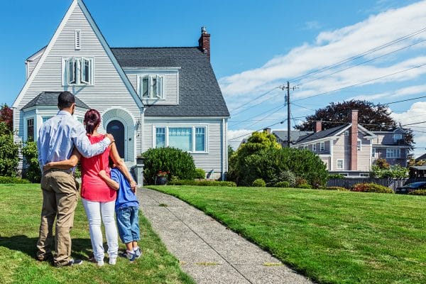 Photo of a young mixed-race family admiring a home - possibly their first home, or the home they hope to own.