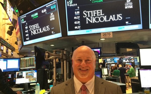 Ben Plotkin poses for a photo on the NYSE stock exchange floor under a sign with the Stifel trading price and analytics.