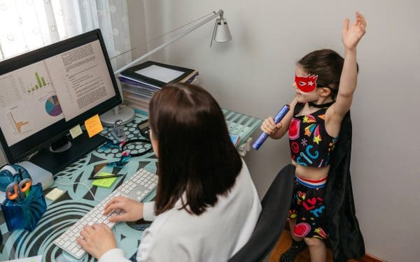 Top view of woman working from home with her daughter singing and playing by her side. Selective focus on girl in background