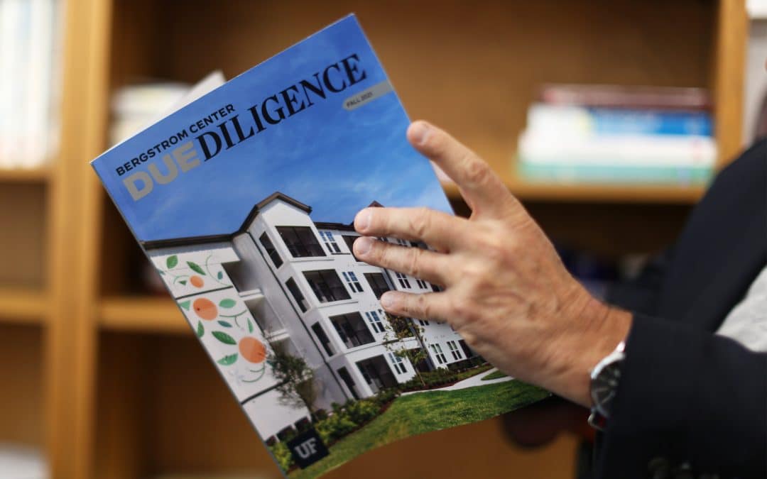 Man's hand holding the cover of UF's Due Diligence magazine.