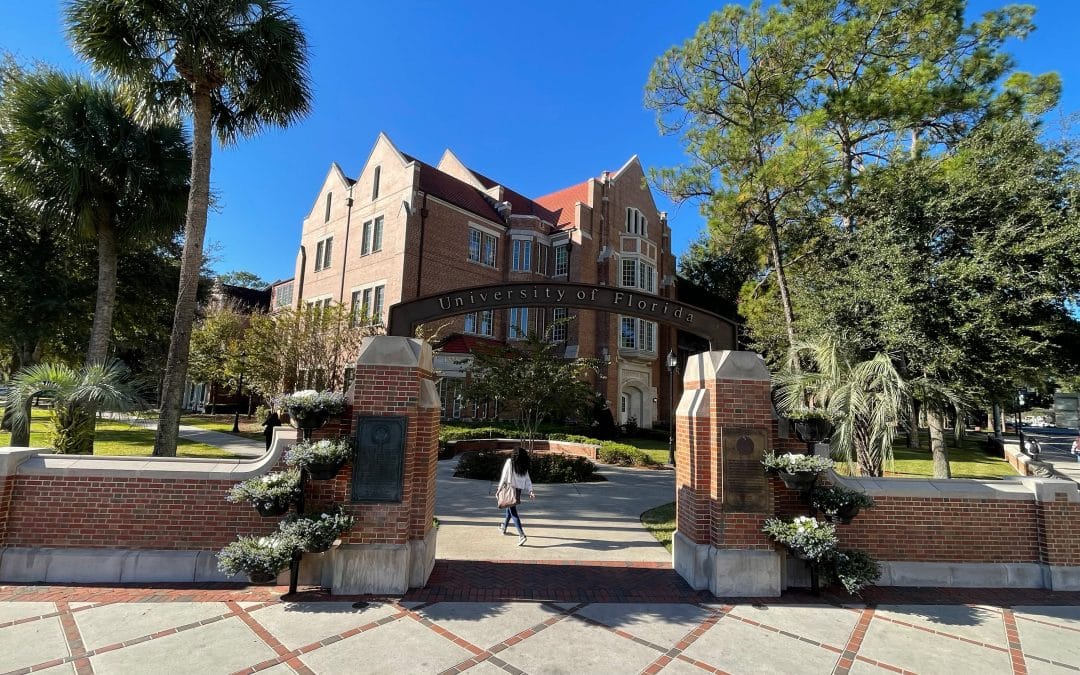Heavener Hall behind the University of Florida Archway with a student walking underneath the arch.