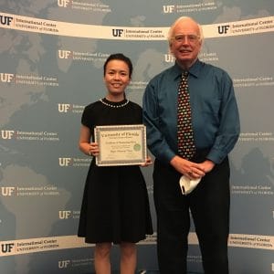 Ngoc Tran holds an award from the UF International Center. She poses for a photo with a man.