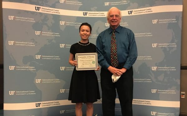 Ngoc Tran holds an award from the UF International Center. She poses for a photo with a man.