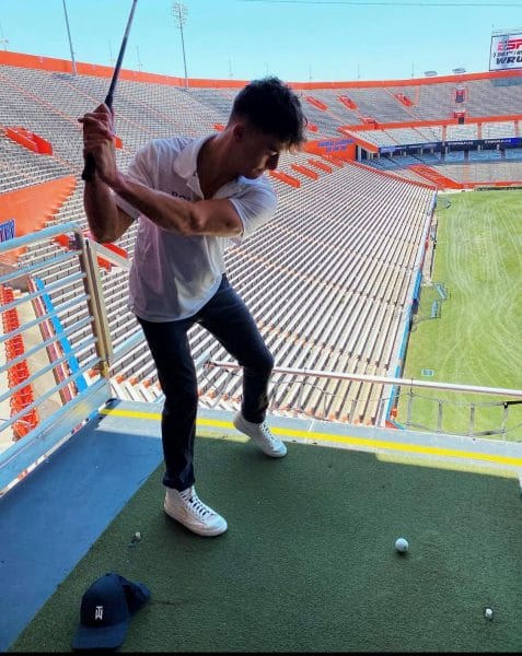 Drew Marshall swinging a golf club in a football stadium. 