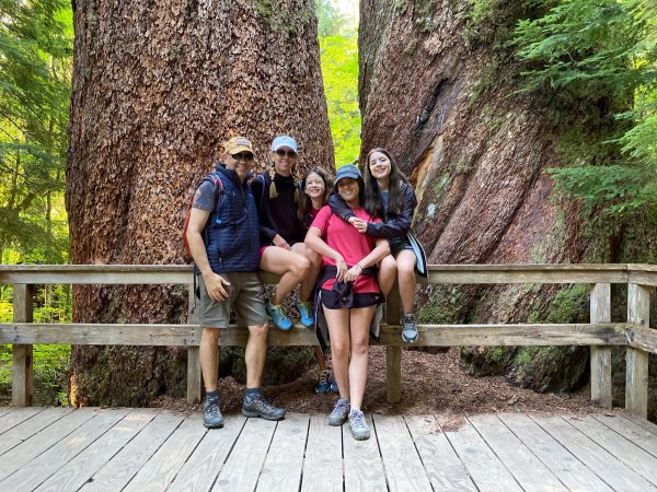 A family of five, father, mother and three daughters pose for a photo in a wooded national park. 