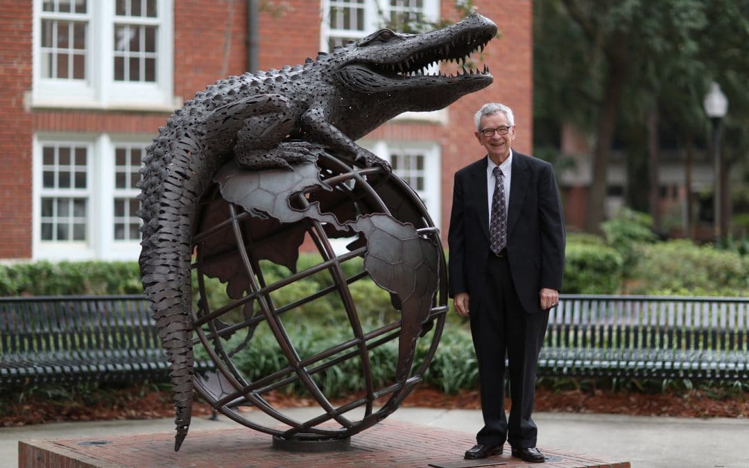 Wayne Archer stands next to a large statue of a gator laying on top of a globe