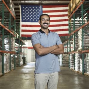 David Habib stands in a warehouse with an American flag behind him.