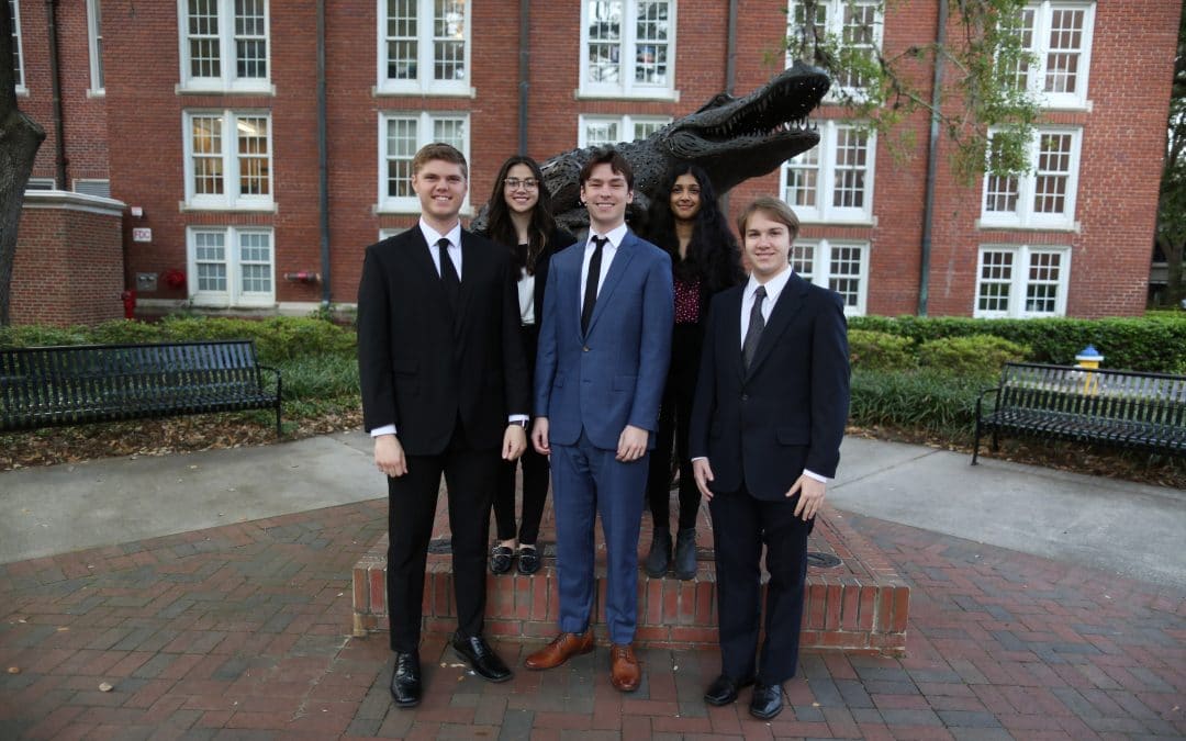 A group of students in suits pose for a photo in front of a large bronze statue of a Gator on a globe.