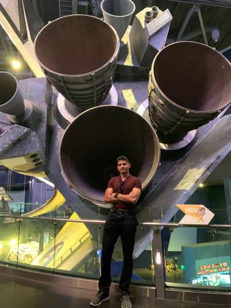 Alexis Munguia stands in front of the bottom of a space shuttle