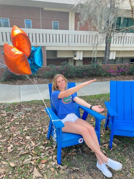 Carolyn Kosuch sits in a blue chair while doing a Gator Chomp.