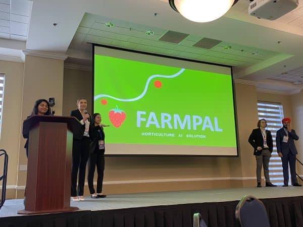 A group of five students stand on a stage to present Farmpal.